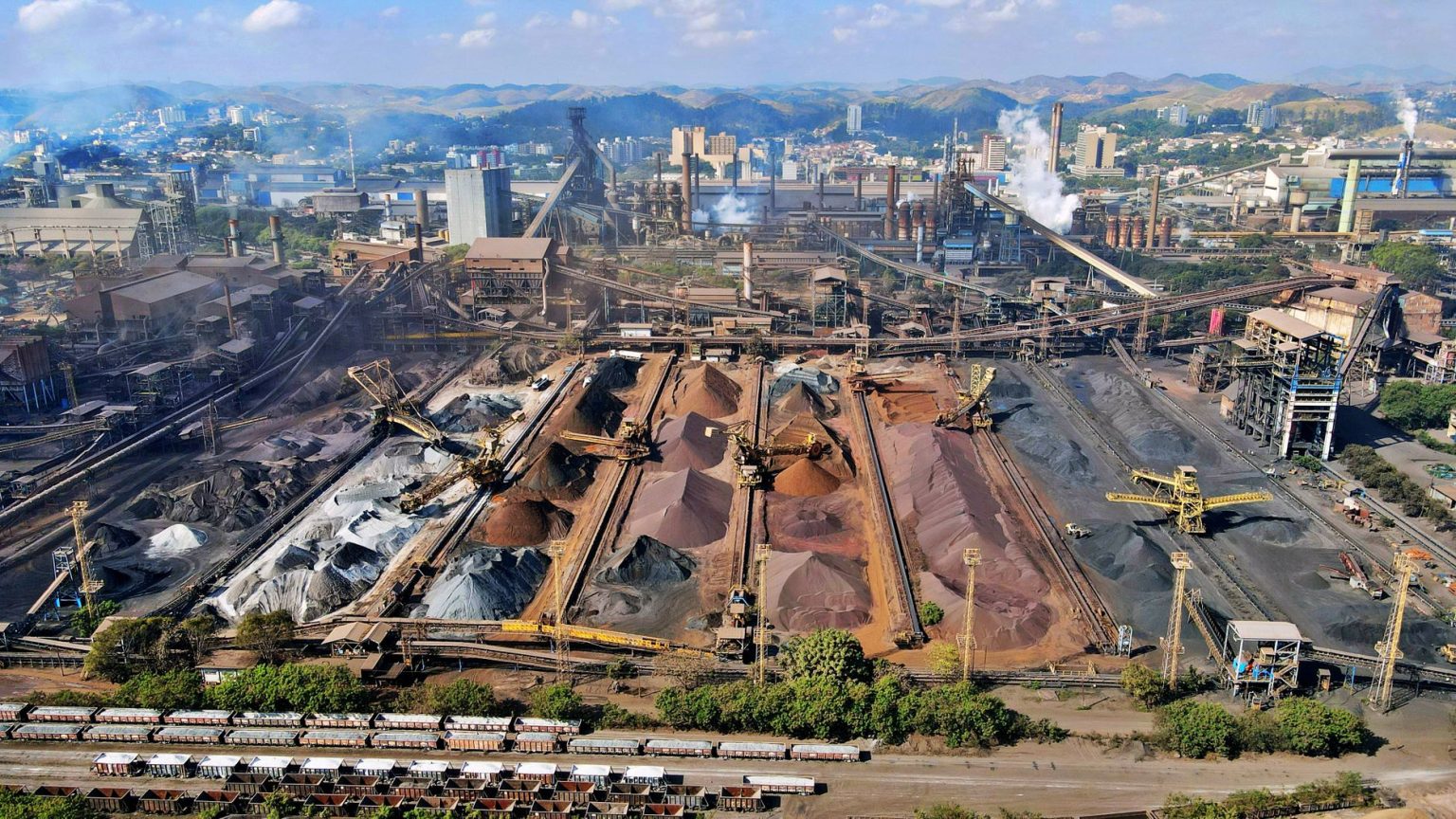 Vista aérea de uma ampla instalação de mineração industrial, com máquinas e pilhas de rejeitos.