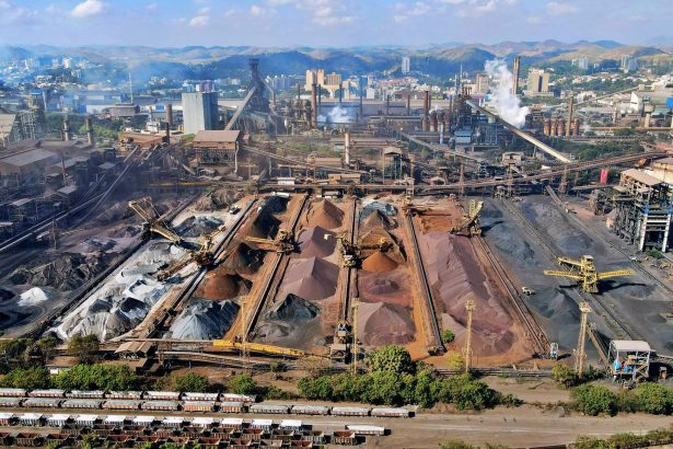 Vista aérea de uma ampla instalação de mineração industrial, com máquinas e pilhas de rejeitos.