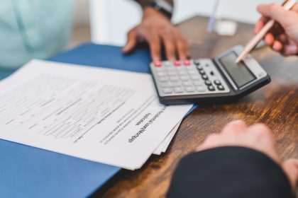Mãos usando uma calculadora sobre documentos imobiliários em uma mesa de trabalho.